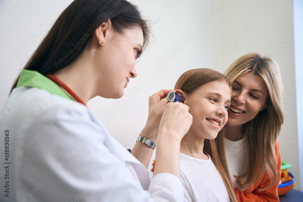 ENT specialist using otoscope with light to check ear to girl patient