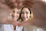 Positive teenage kid and mature grandma showing hand heart, symbol of love, affection, family bonding, looking at camera through finger frame, smiling, laughing, having fun, posing for close up shot