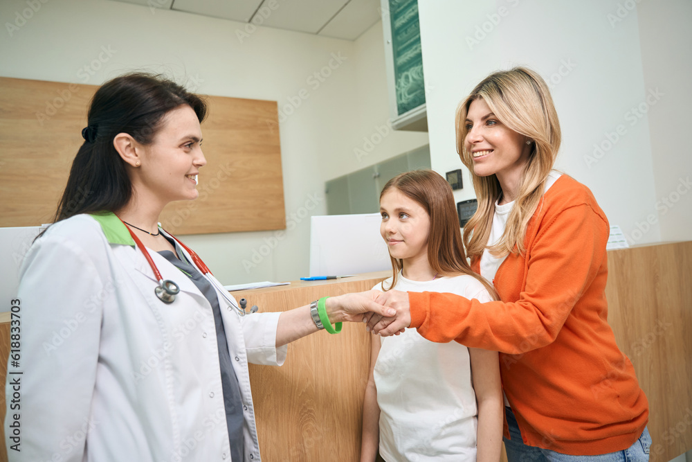 Mother of little patient shaking hand to female pediatrician - obrazy, fototapety, plakaty 