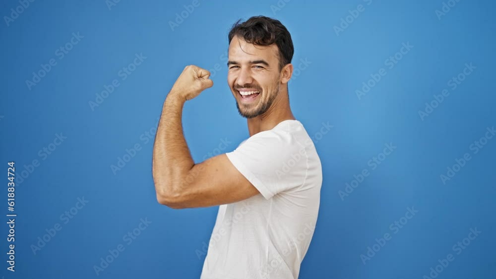 Young hispanic man smiling confident doing strong gesture with arm over isolated blue background