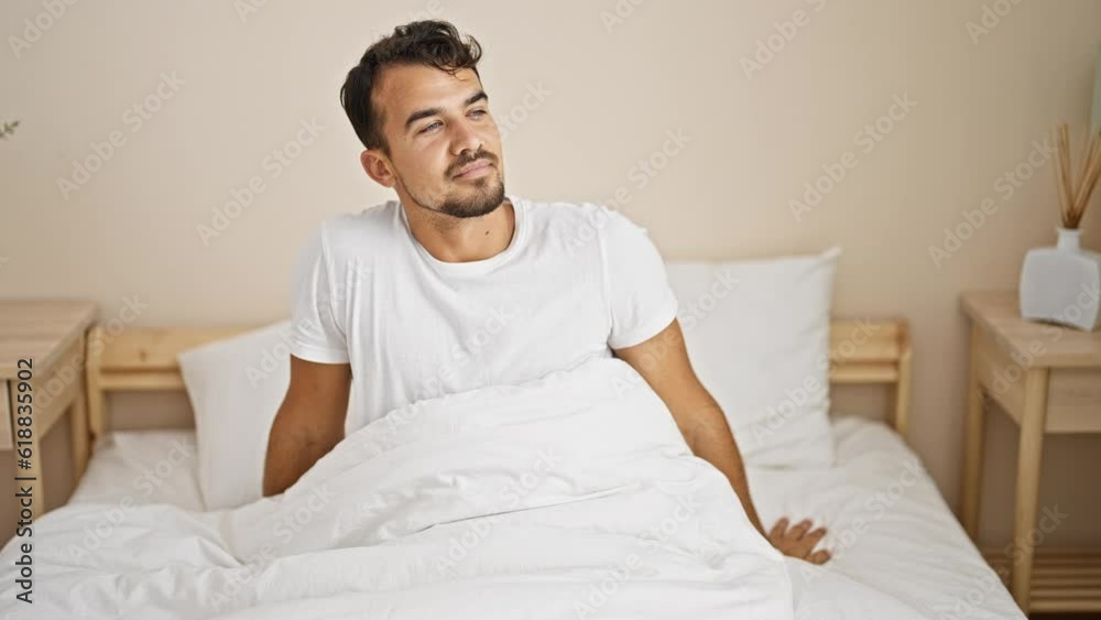 Young hispanic man waking up sitting on bed at bedroom Young hispanic man waking up sitting on bed at bedroom