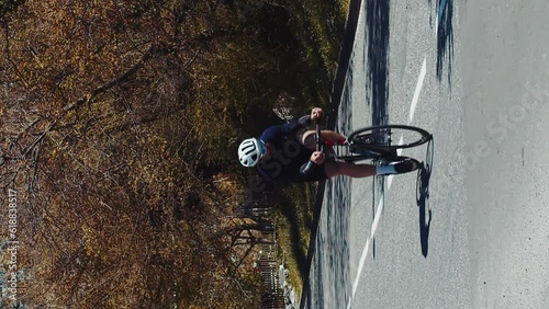 Vertical shot professional cyclist riding a bike on asphalt road, sportsman cycling on road outdoors in beautiful countryside landscape