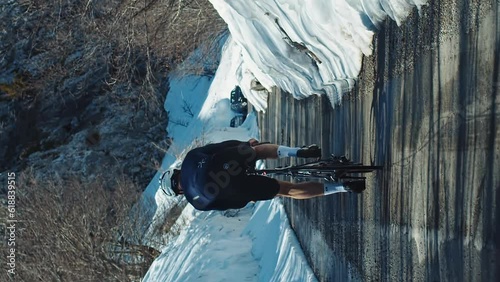 Vertical shot cyclist rides on a mountain snowy road among high mountains, a lone sportsman cycling on road, cycling sport workout concept