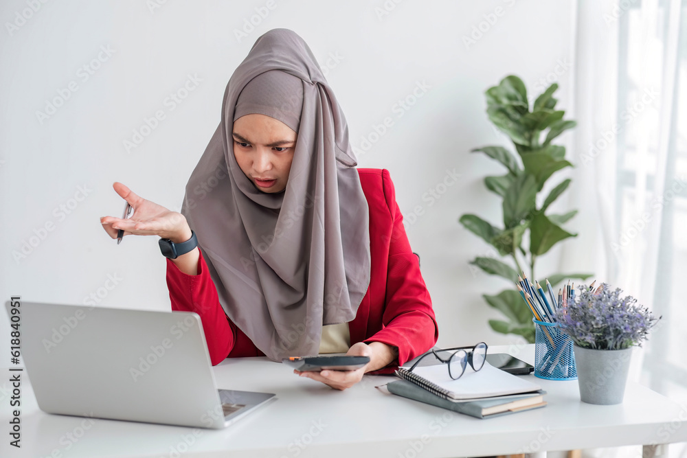 Serious young woman wearing hijab sitting at desk working on new business project alone in modern office