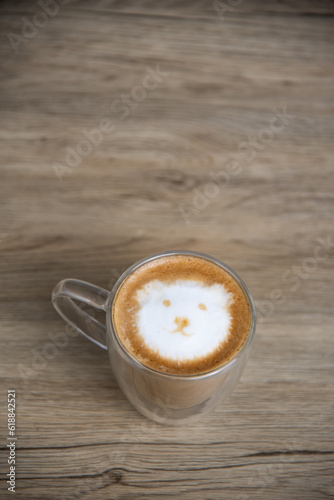 A hot latte with milk froth painted in the shape of a bear's face on wood table