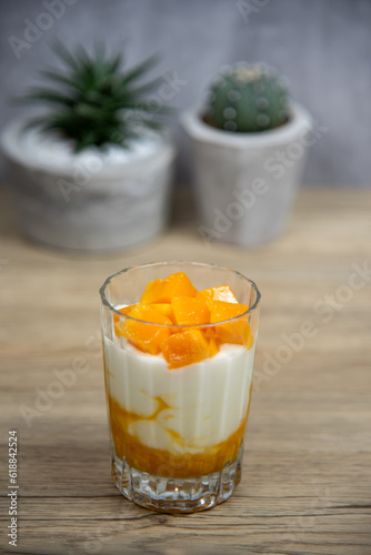 A glass of ripe mangoes with yoghurt on a wood table