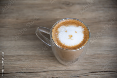 A hot latte with milk froth painted in the shape of a bear's face on wood table