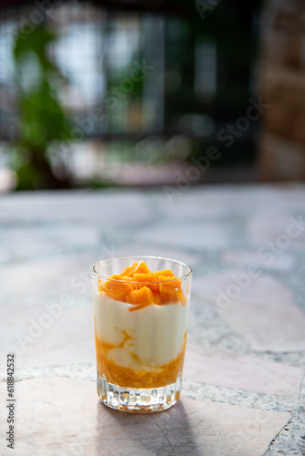 A glass of ripe mangoes with yoghurt on a cement table