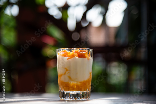 A glass of ripe mangoes with yoghurt on a cement table