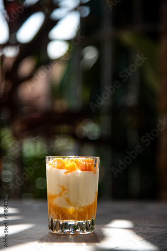 A glass of ripe mangoes with yoghurt on a cement table