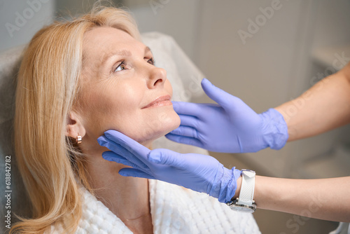 Hands in medical gloves touching happy woman face