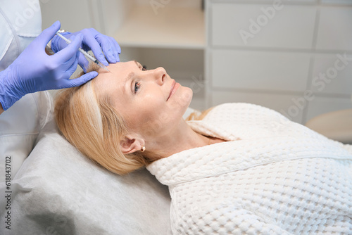 Close up of happy adult woman getting face antiwrinkle injection