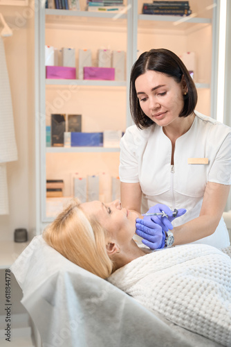 Smiling beautician performing injection on lady chin