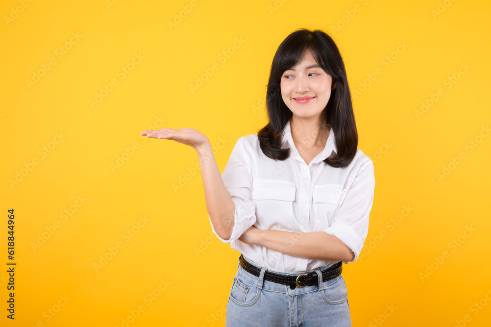 Happy young asian woman wearing white shirt and denim jean plants presenting or showing open hand palm with copy space for product isolated on yellow background. Present product advertising concept. Happy young asian woman wearing white shirt and denim jean plants presenting or showing open hand palm with copy space for product isolated on yellow background. Present product advertising concept.