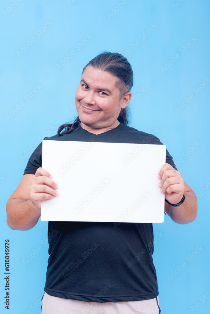 A biracial male with undercut holding a blank placard while doing a head tilt and smiling. Isolated on a blue background. A biracial male with undercut holding a blank placard while doing a head tilt and smiling. Isolated on a blue background.