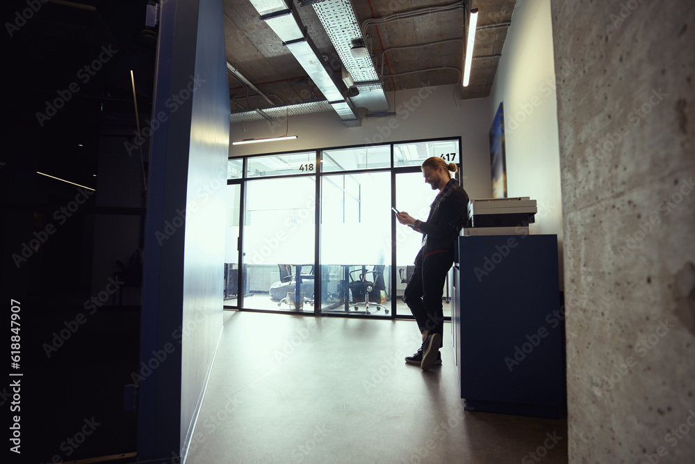 Man in casual clothes stands with a phone at copier Man in casual clothes stands with a phone at copier