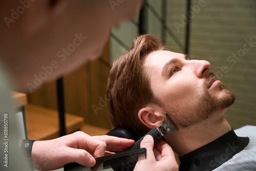 Master cuts the beard of a young client in abarbershop