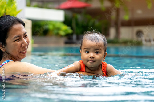 Smiling Asian little girl with mother in swimming pool., concept of relax and healthy family