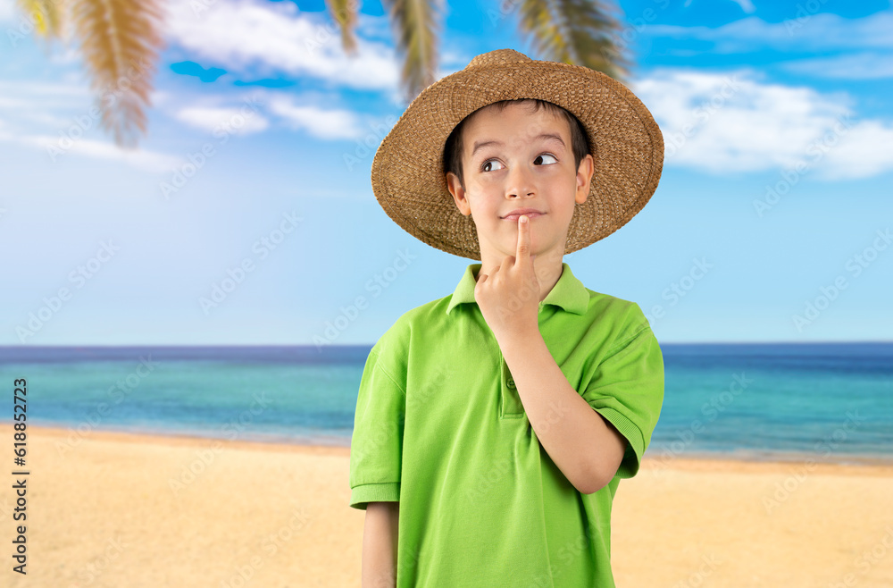 Little boy wearing green t-shirt and hat at beach with hand on chin thinking about question, thoughtful expression. Smiling with thoughtful face. Doubt concept.