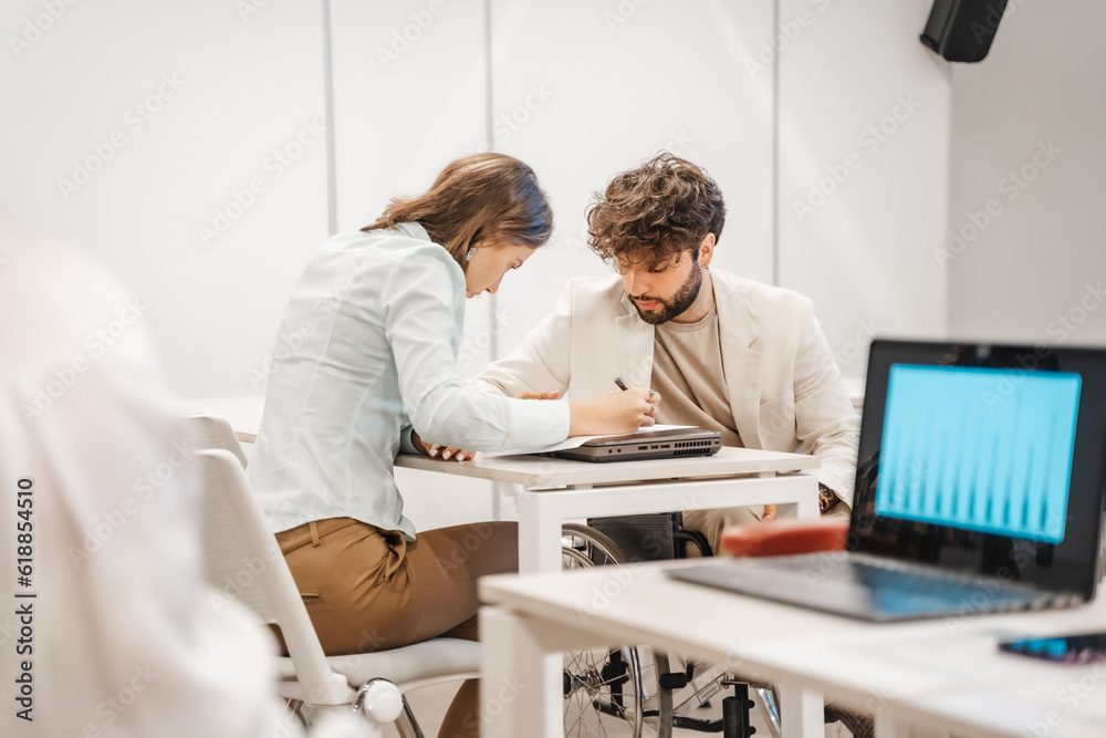 Handicapped male employee in wheelchair working together with his brunette female coworker