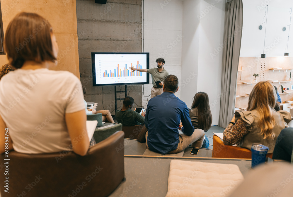 Obraz premium Sales discussion. Good looking male employee explaining profit growth to his coworkers at modern meeting room