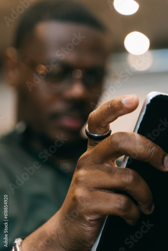 Blurred photo of black male chatting on tablet. Focus on hands and tablet
