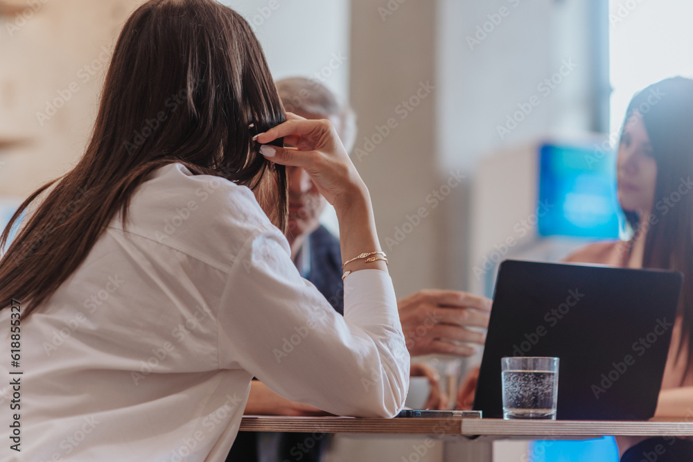 Back view photo of young female employee working with his experienced coworkers. Senior experienced businessman teaching young employees at the office