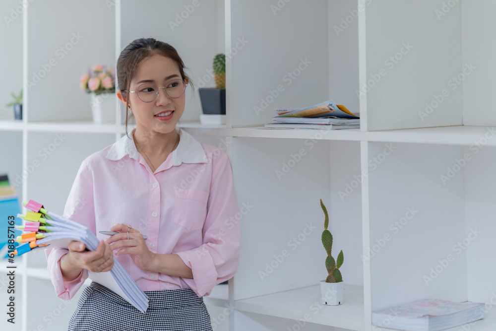 Image of smiling beautiful woman writing down notes while sitting at table in office Image of smiling beautiful woman writing down notes while sitting at table in office