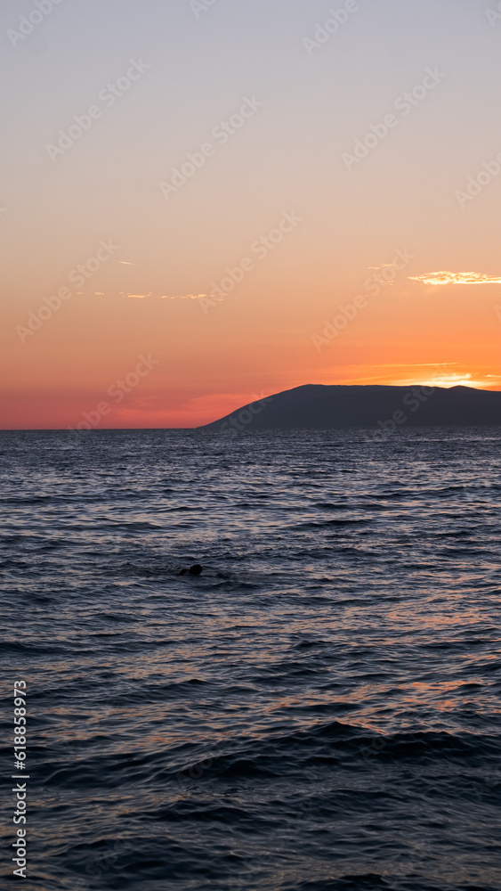 Ocean small waves on sunset lights.
Sun sitting  over the island. Beautiful view from evening beach.