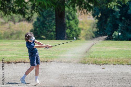 A Kid hitting the ball out of the bunker