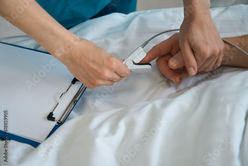 Doctor putting pulse oximeter onto male patient finger in clinic photo