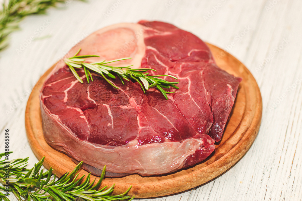 Fototapeta premium Fresh piece of meat large beef steak on the bone ossobuco with rosemary sprig.
