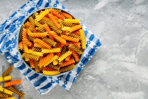 Tricolor fusilli pasta in bowl on a gray background. Fusilli dry pasta on a linen napkin. Copy space