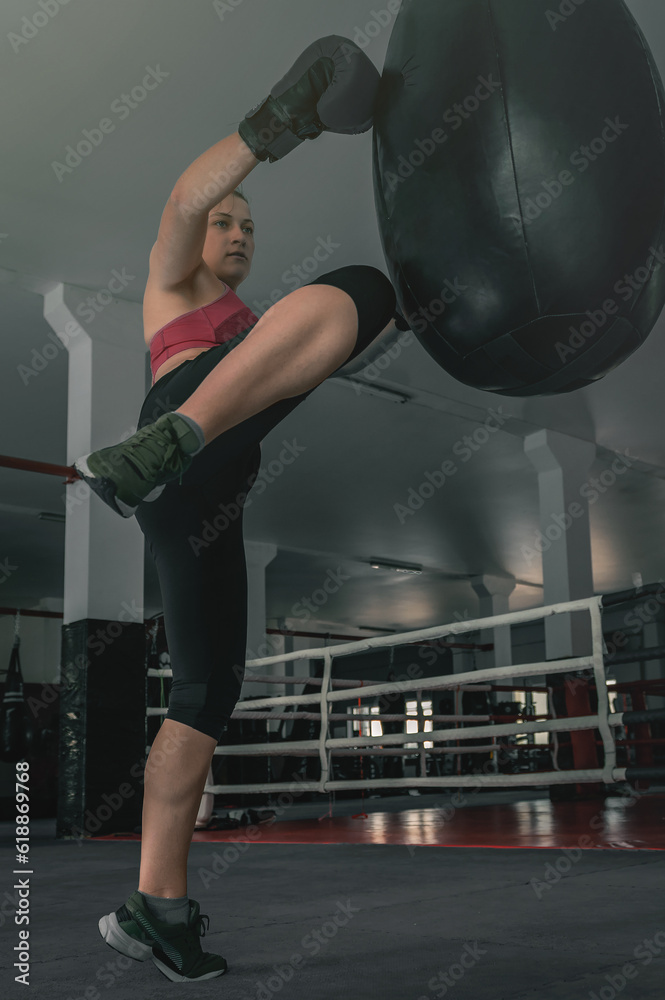Women's self-defense force. Young female kickboxer is training with a punching bag in the gym.