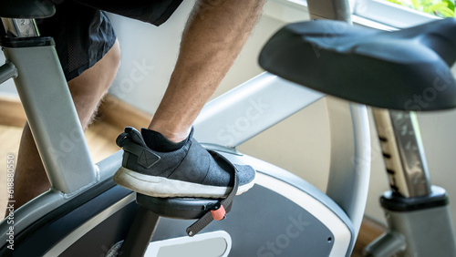 Close up of male feet in sport footwear cycling on an upright stationary bike or upright exercise bicycle. Indoor cardio training workout and burn calories in fitness gym photo