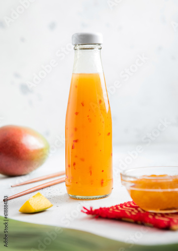 Mango sauce in glass bottle on light background with fresh fruits.