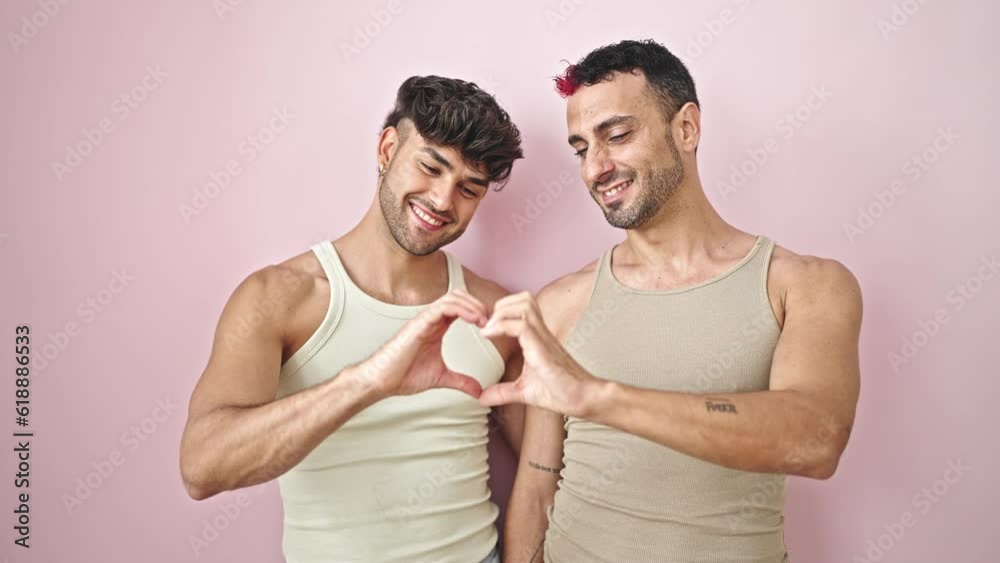 Two men couple hugging each other doing heart gesture over isolated pink background Two men couple hugging each other doing heart gesture over isolated pink background