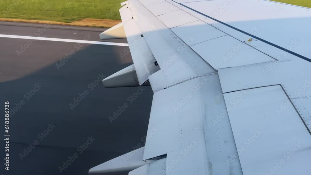 Travel video from the airplane window during takeoff. The aircraft wing and the runway through the passenger's eyes through the porthole on a clear sunny day. High quality 4k footage