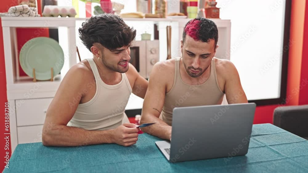 Two men couple shopping with laptop and credit card sitting on table at dinning room Two men couple shopping with laptop and credit card sitting on table at dinning room