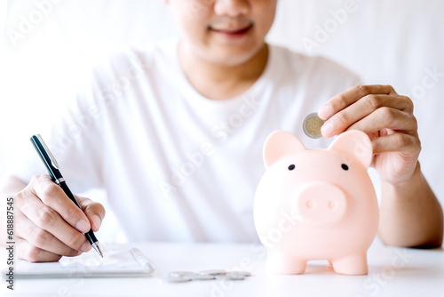A young man was happy to use a coin to put a piggy bank into a piggy bank and take notes. concept of saving money for investment