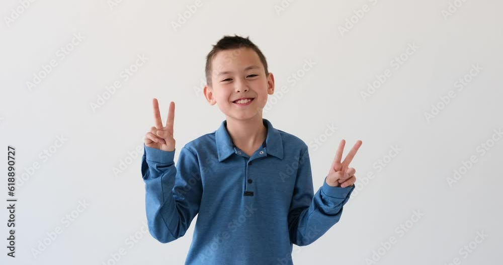 Asian schoolboy displays the iconic Victory gesture on white backdrop. With a beaming smile and outstretched fingers forming the victory sign, this young boy radiates positivity and enthusiasm. Asian schoolboy displays the iconic Victory gesture on white backdrop. With a beaming smile and outstretched fingers forming the victory sign, this young boy radiates positivity and enthusiasm.