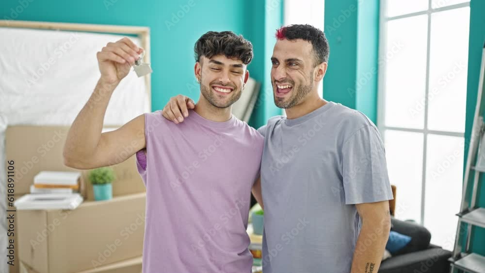 Two men couple hugging each other holding keys at new home Two men couple hugging each other holding keys at new home