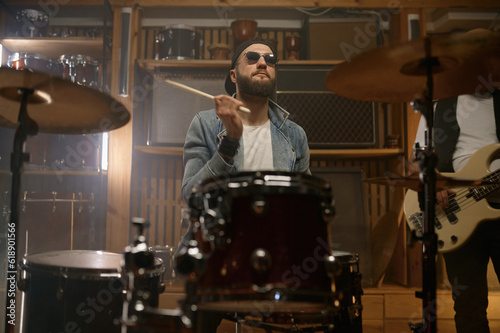 Stylish drummer playing music during rock band indoor club performance