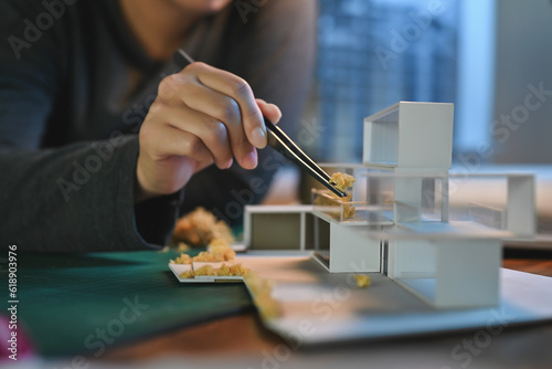Close-up hand of Architect students diligently make house model building samples with paper art architecture tools at night in their alone room.