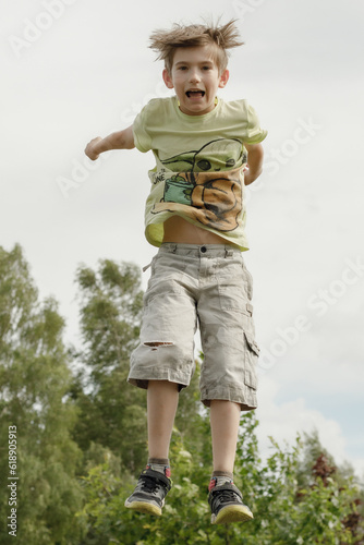 A child jumps on a trampoline. The air hung in the boy's jump. A child with positive emotions jumps © Emvats