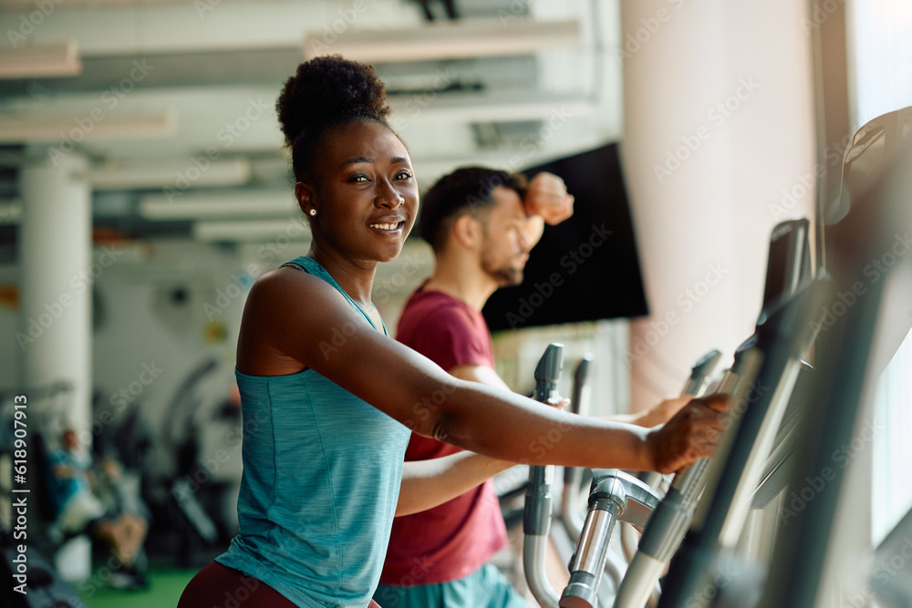 Fototapeta premium Happy black athletic woman using cross trainer machine while exercising in gym.