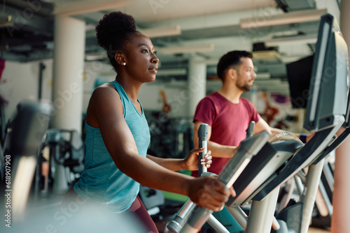 Young black sportswoman using elliptical trainer while exercising in gym. photo