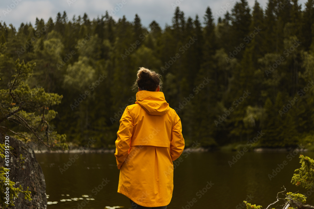 A caucasian woman hiker standing by a lake in a forest wearing a yellow jacket.