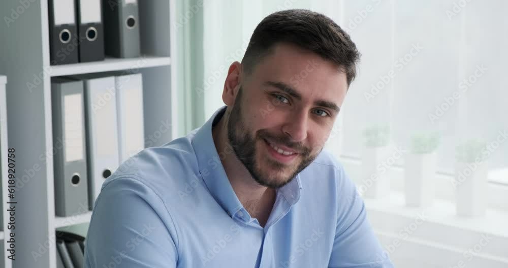 Optimistic Caucasian businessman in a crisp shirt sits at his desk in the office, smiling broadly at the camera with his perfect teeth, exuding charm and charisma. Optimistic Caucasian businessman in a crisp shirt sits at his desk in the office, smiling broadly at the camera with his perfect teeth, exuding charm and charisma.