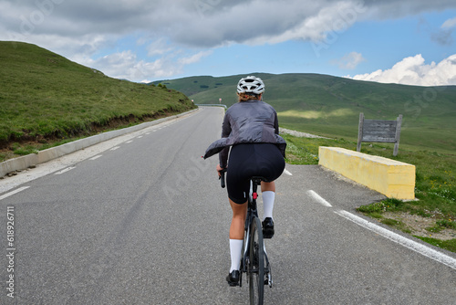 Female cyclist riding a road bike with a view of the mountains.Training for competition.Practicing cycling on open country road. Bucegi Natural Park. photo